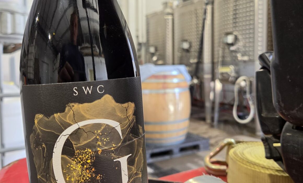 Bottle of Stiekema 2022 Grenache in a Paso Robles winery cellar with barrels and tanks